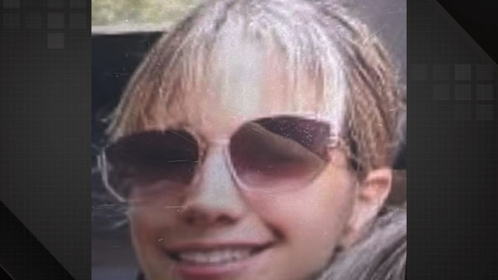 Close-up do rosto de uma mulher sorrindo, usando óculos de sol grandes e cabelo claro