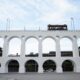 Arcos da Lapa brancos com bonde amarelo sobre a estrutura e céu azul