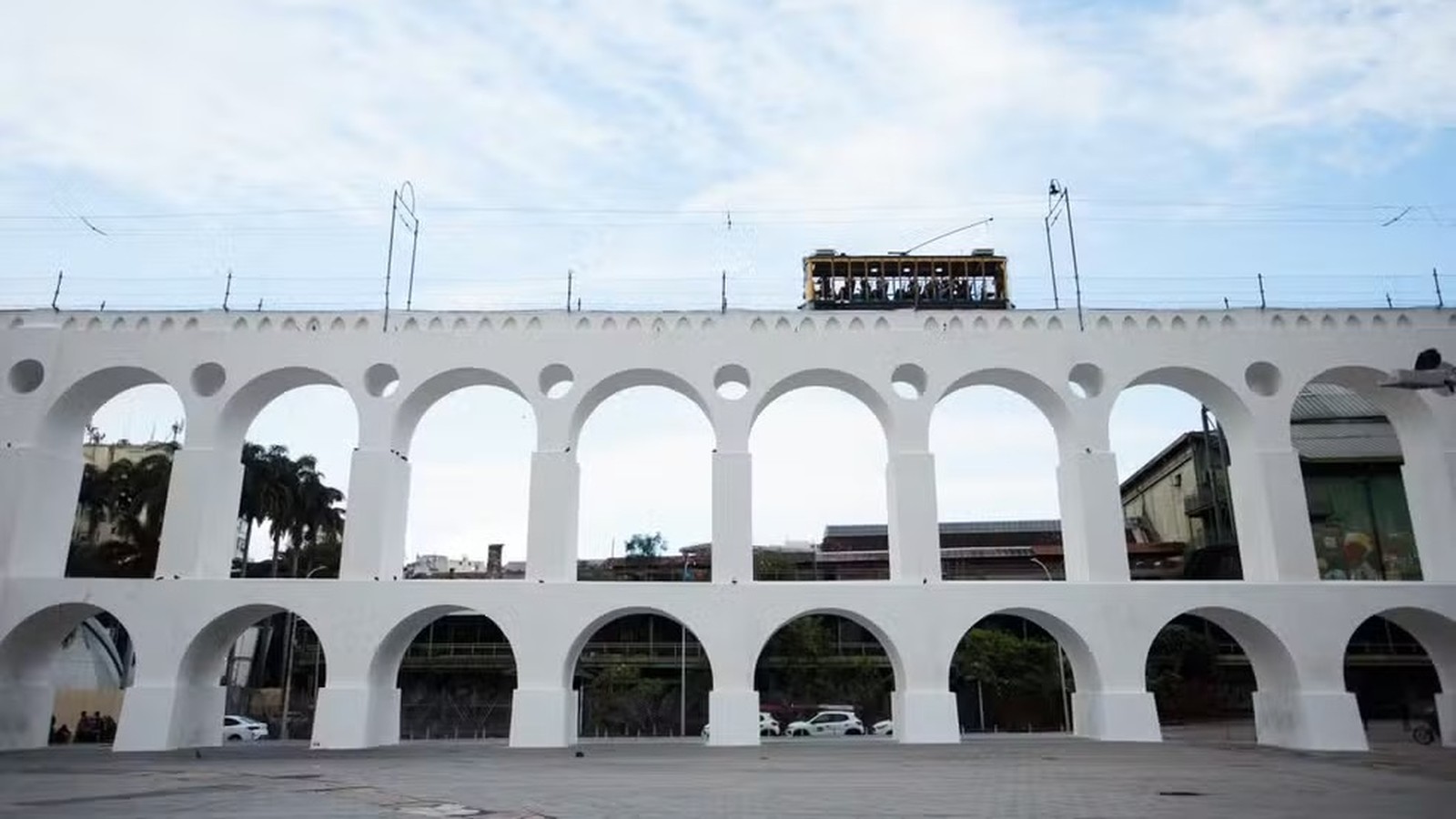 Arcos da Lapa brancos com bonde amarelo sobre a estrutura e céu azul