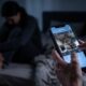Mãos seguram smartphone exibindo aplicativo de segurança com visão ao vivo de fumaça e pessoa no fundo escuro.