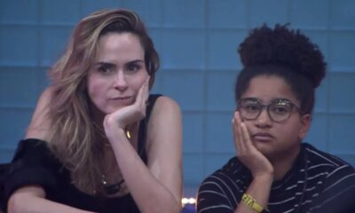Duas mulheres, uma loira e uma de cabelo cacheado com óculos, olhando para frente