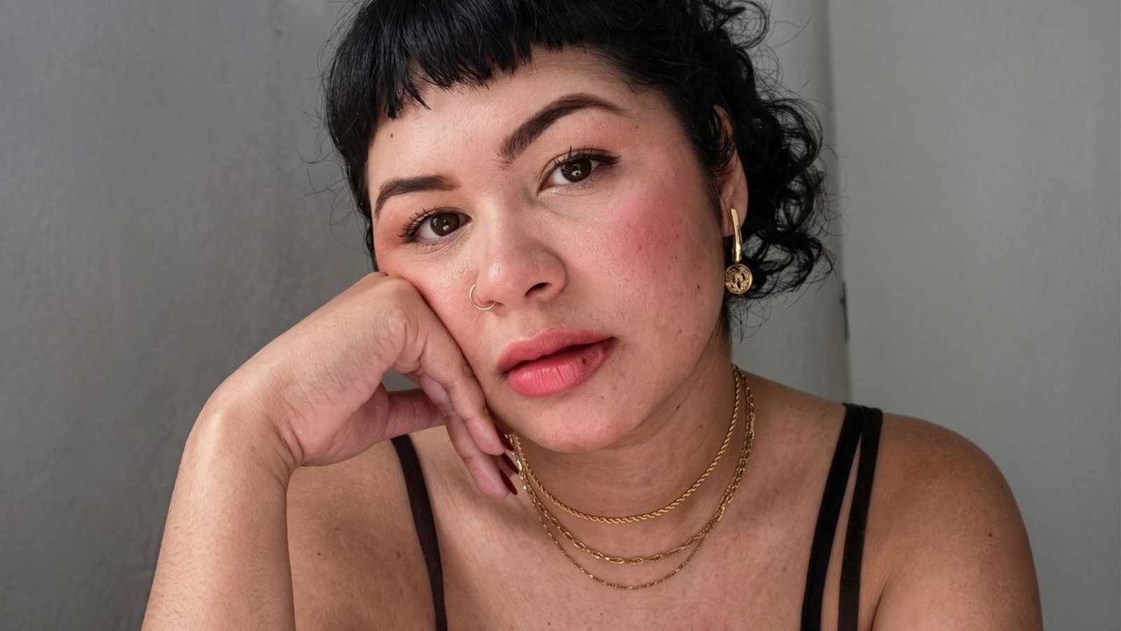 Close-up retrato de mulher com cabelo escuro cacheado, argola no nariz e colares dourados