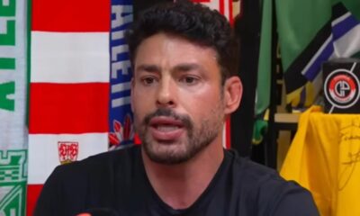 Cauã Reymond de perto, falando ao fundo cachecóis e logo Charla Podcast