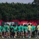 Jogadores de futebol em huddle no campo de treino, com placa SUPERBET e árvores