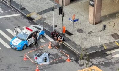 Viatura policial, policial, três homens sentados na calçada e cena de acidente isolada com cones na rua