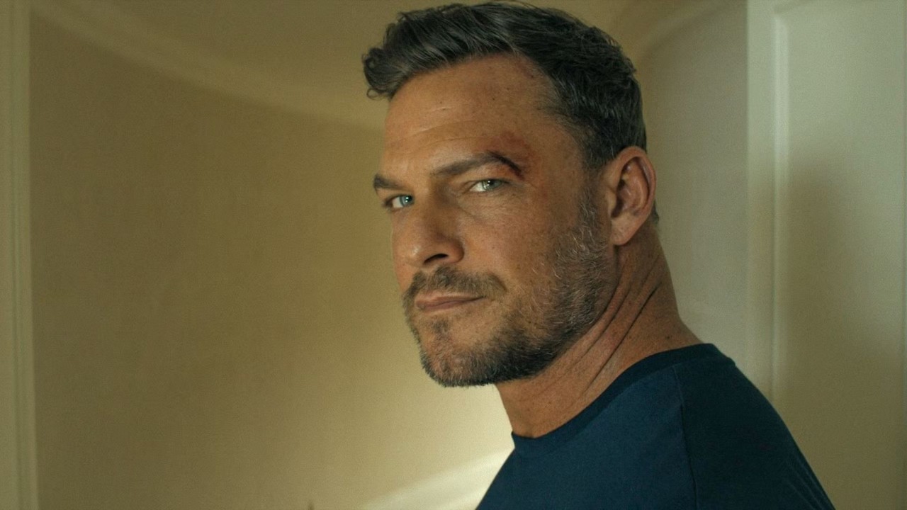 Alan Ritchson com barba e arranhão na testa, olhando para a câmera.