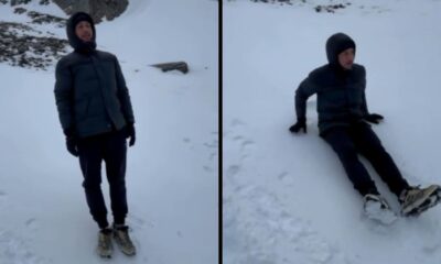 Homem com jaqueta escura em pé e depois sentado na neve em paisagem montanhosa