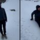 Homem com jaqueta escura em pé e depois sentado na neve em paisagem montanhosa