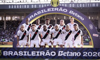 Jogadores do Vasco em campo, uniformizados, sob arco com 'Brasileirão Betano 2026'.