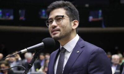 Kim Kataguiri de óculos, camisa xadrez e gravata, discursa ao microfone em plenário