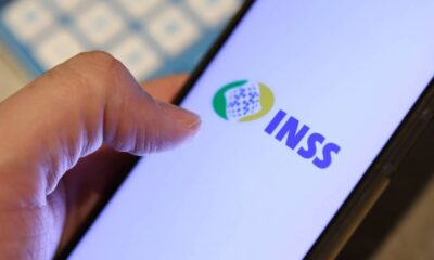 Uma mão segura um smartphone com o logotipo e o nome "INSS" em destaque na tela do aparelho.