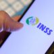 Uma mão segura um smartphone com o logotipo e o nome "INSS" em destaque na tela do aparelho.