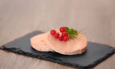 Duas fatias de foie gras em um prato de ardósia, guarnecidas com groselhas vermelhas e ervas
