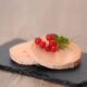 Duas fatias de foie gras em um prato de ardósia, guarnecidas com groselhas vermelhas e ervas