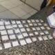 Drogas em sacolas, notas de dinheiro e placa da Polícia Militar sobre bancada