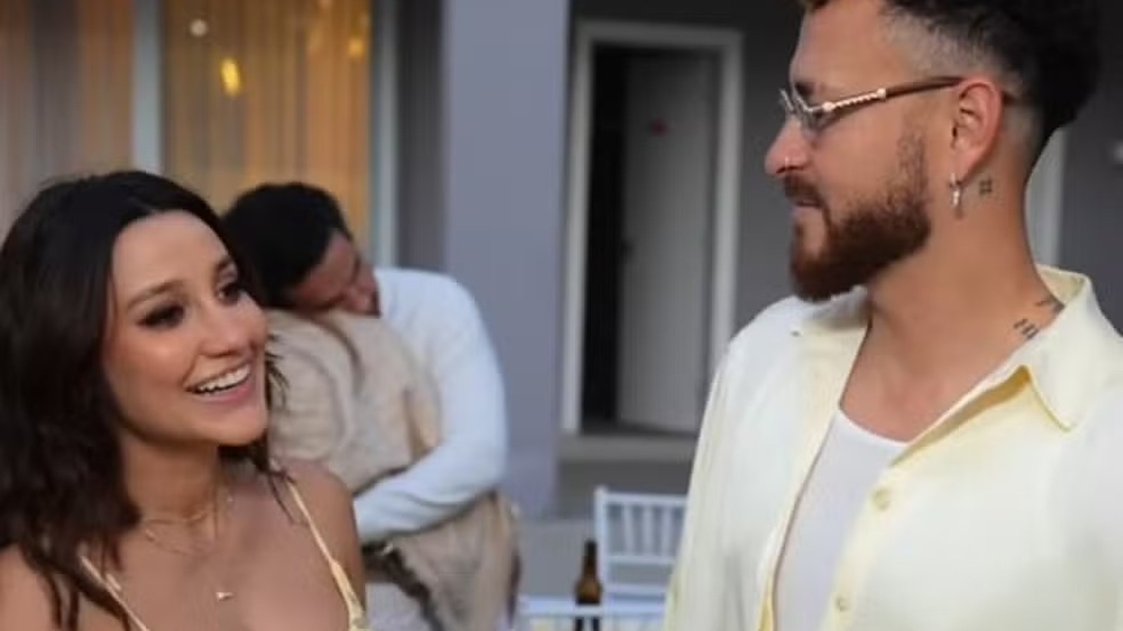 Fred Bruno e Indi sorrindo e se olhando; homem em segundo plano