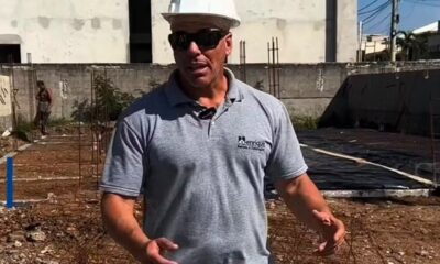 Homem de capacete branco, óculos escuros e camisa cinza com logo 'Henrique Projetos e Construção' em obra