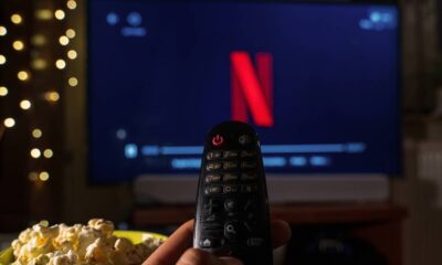 Mão segura controle remoto apontado para TV exibindo o logo Netflix, com pipoca