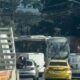 Trânsito intenso com ônibus, caminhão, van, carro e táxi amarelo em rua urbana