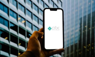 Mão segura smartphone com logo PIX na tela. Edifício moderno com janelas ao fundo