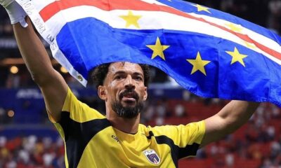 Homem de barba, usando camisa de goleiro amarela e preta, ergue a bandeira de Cabo Verde