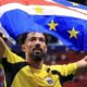 Homem de barba, usando camisa de goleiro amarela e preta, ergue a bandeira de Cabo Verde