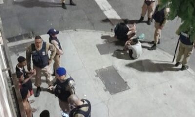 Agentes de segurança uniformizados detendo dois indivíduos na calçada à noite