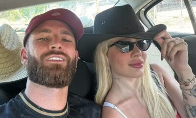 Selfie de casal no carro: homem de boné, mulher loira de chapéu e óculos escuros