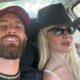 Selfie de casal no carro: homem de boné, mulher loira de chapéu e óculos escuros