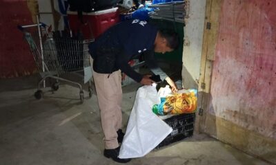 Homem em depósito inspeciona mercadorias apreendidas com saco e lanterna do celular