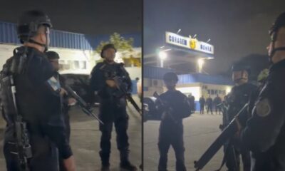 Policiais militares fardados com capacetes e fuzis em operação noturna, sob placa "CORAGEM"
