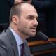 Eduardo Bolsonaro, homem branco com barba, terno cinza, falando em um microfone