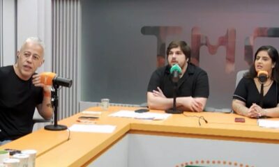 Alexandre Frota e dois apresentadores em estúdio de podcast, com microfones e mesa laranja
