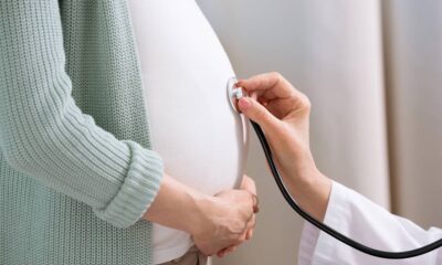 Mão de profissional com estetoscópio examinando barriga de gestante