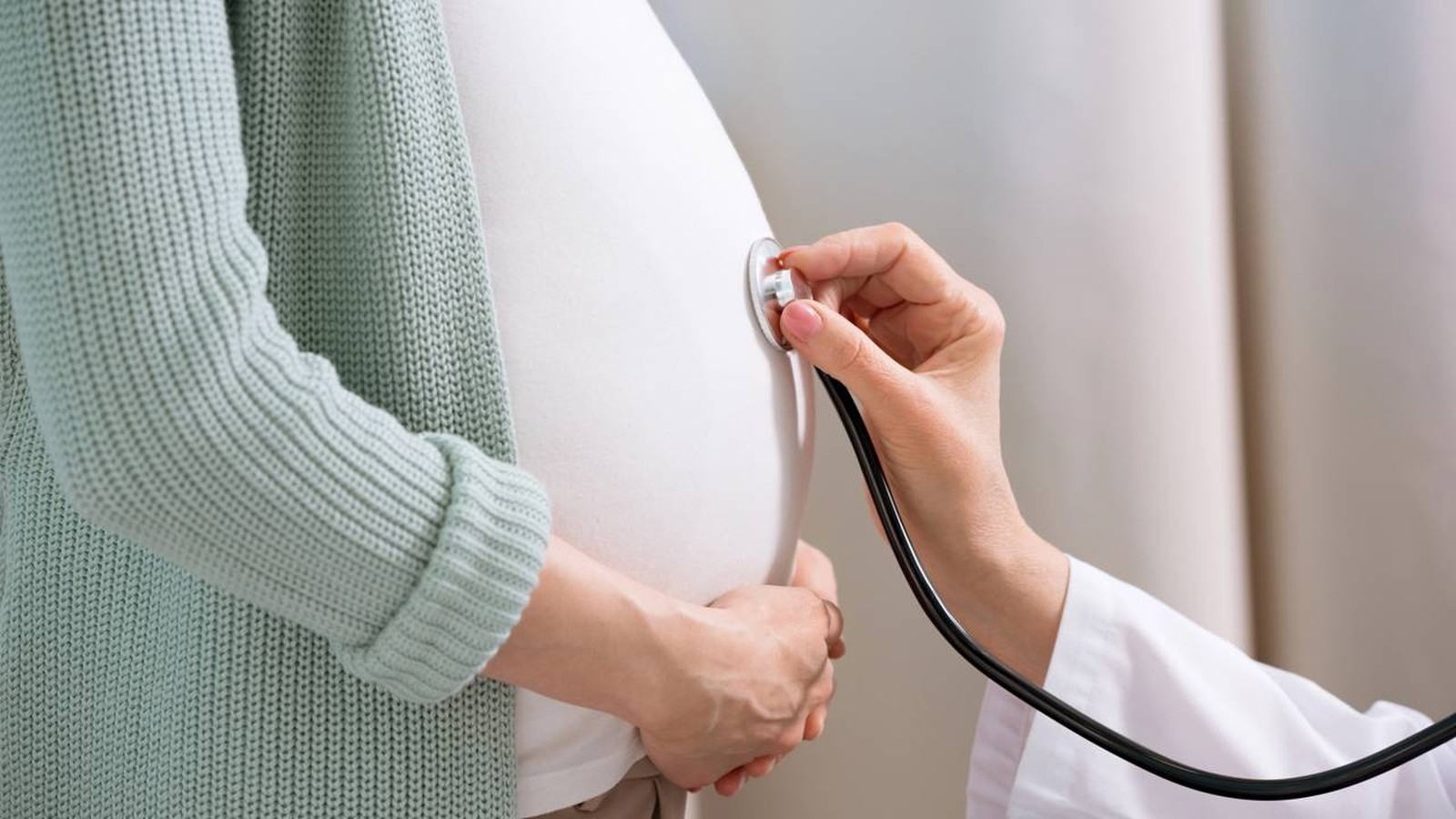 Mão de profissional com estetoscópio examinando barriga de gestante