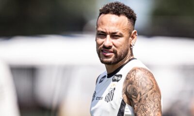Jogador Neymar em close, sorrindo, camisa regata do Santos, com tatuagens no braço