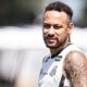 Jogador Neymar em close, sorrindo, camisa regata do Santos, com tatuagens no braço