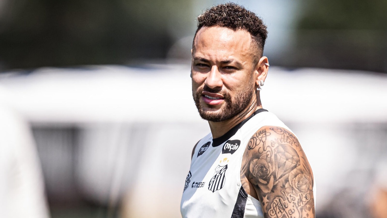Jogador Neymar em close, sorrindo, camisa regata do Santos, com tatuagens no braço