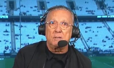 Galvão Bueno com óculos e fone de ouvido com microfone, em cabine de transmissão de estádio, com 'neo química' no fundo.