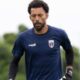 Goleiro de barba e cabelo cacheado, vestindo uniforme azul e luvas, em campo.