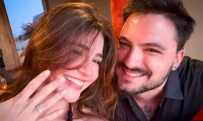 Mulher e homem sorrindo, ela exibe anel de noivado na mão esquerda