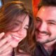 Mulher e homem sorrindo, ela exibe anel de noivado na mão esquerda