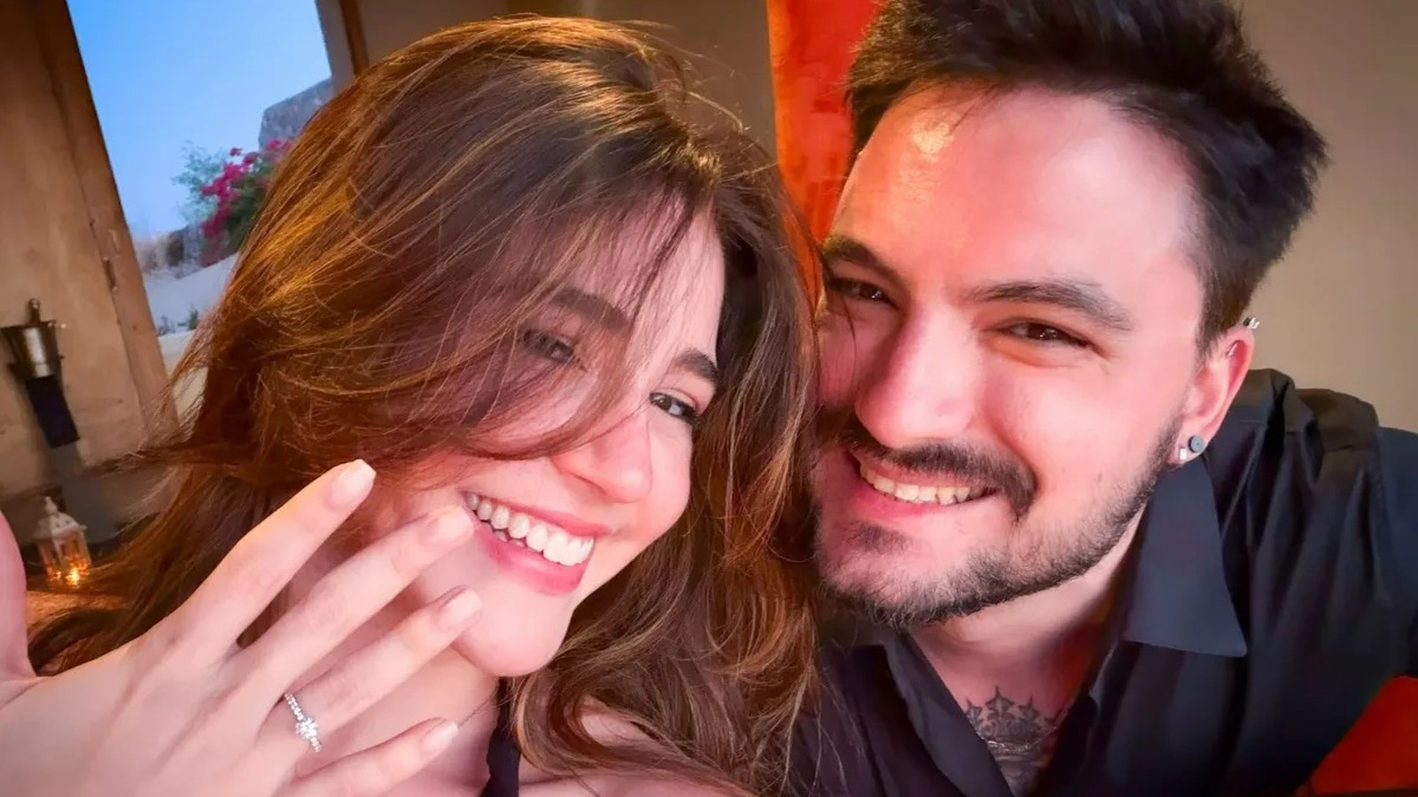Mulher e homem sorrindo, ela exibe anel de noivado na mão esquerda