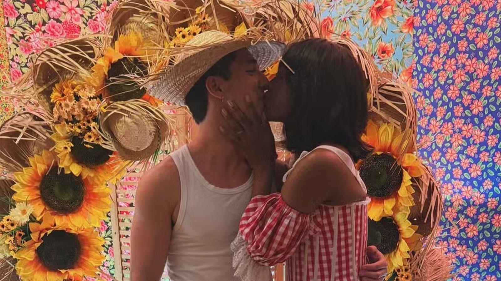 IZA e João Vitor Silva se beijam, ele com chapéu de palha e ela de blusa xadrez, entre girassóis