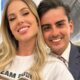 Casal sorrindo para a câmera, homem de terno e mulher de camiseta branca.
