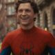 Tom Holland sorridente em traje vermelho e azul do Homem-Aranha, com fundo de cidade desfocado