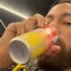 Homem com barba e boné preto bebendo de uma lata de Red Bull amarela e vermelha
