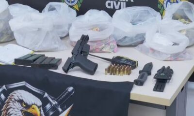 Mesa com pistola, carregadores, munições, rádio, faca, coldre, notas e sacolas plásticas