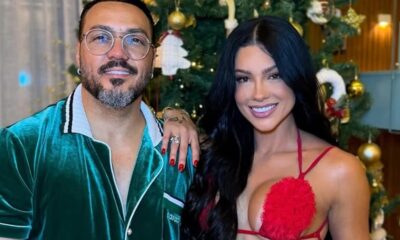 Belo e Rayane Figliuzzi sorrindo lado a lado, em frente a uma árvore de Natal decorada