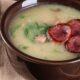 Tigela de caldo verde com linguiça calabresa fatiada, couve e pedaços de carne